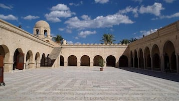 A courtyard with a central open space surrounded by arches, a dome structure, and palm trees.