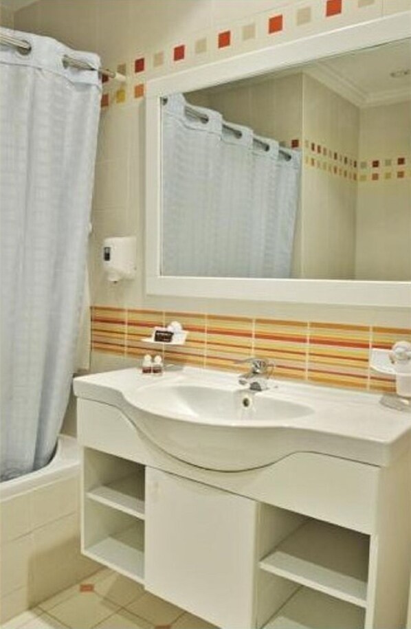 Un baño con lavamanos blanco, espejo y salpicadero con azulejos a rayas.
