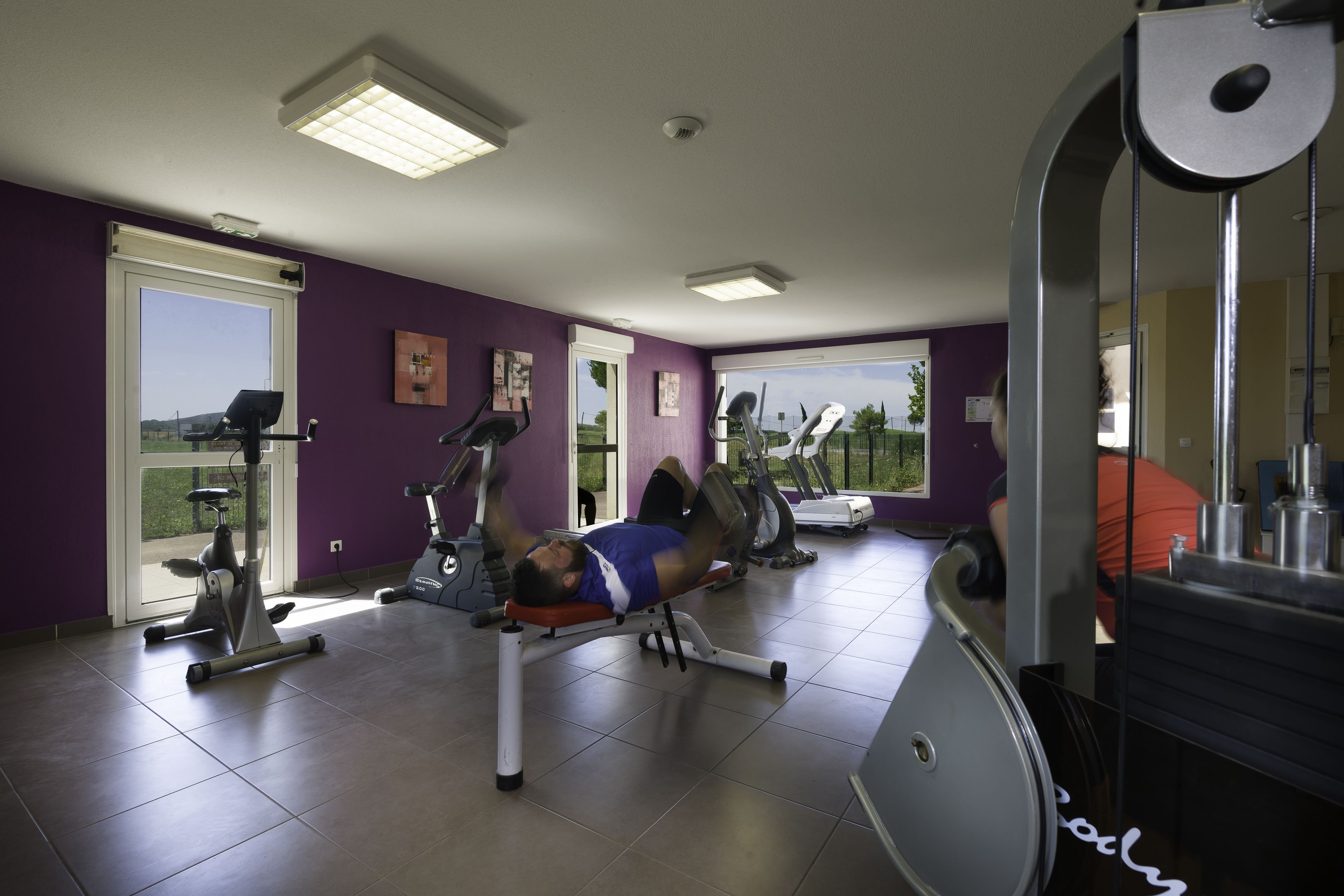 Un gimnasio con equipo de ejercicio, un ventanal grande y una pared morada.