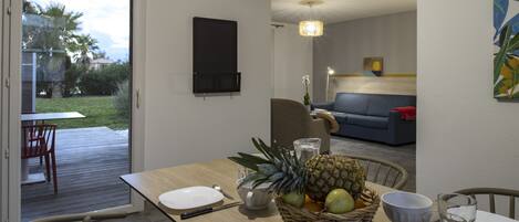 A dining area with a table set for two, a wicker fruit basket, and a view of the outdoor patio.