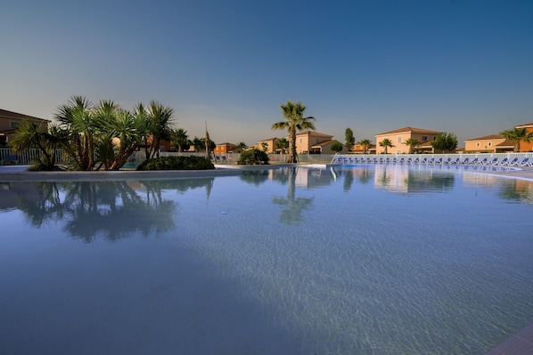 A clear swimming pool surrounded by palm trees and buildings.