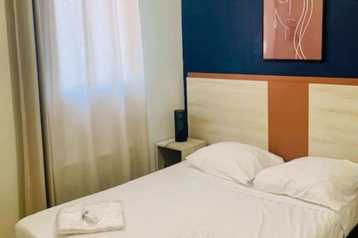 Una habitación de hotel con una cama, una mesita de noche, una obra de arte en la pared y una cortina.