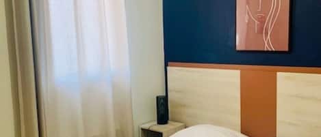 Una habitación de hotel con una cama, una mesita de noche, una obra de arte en la pared y una cortina.