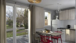Una cocina moderna con comedor, puertas corredizas de vidrio a una terraza y vistas a árboles y una carretera.