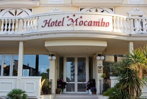 Hotel Mocambo con una entrada destacada, un balcón con barandillas y plantas en macetas.