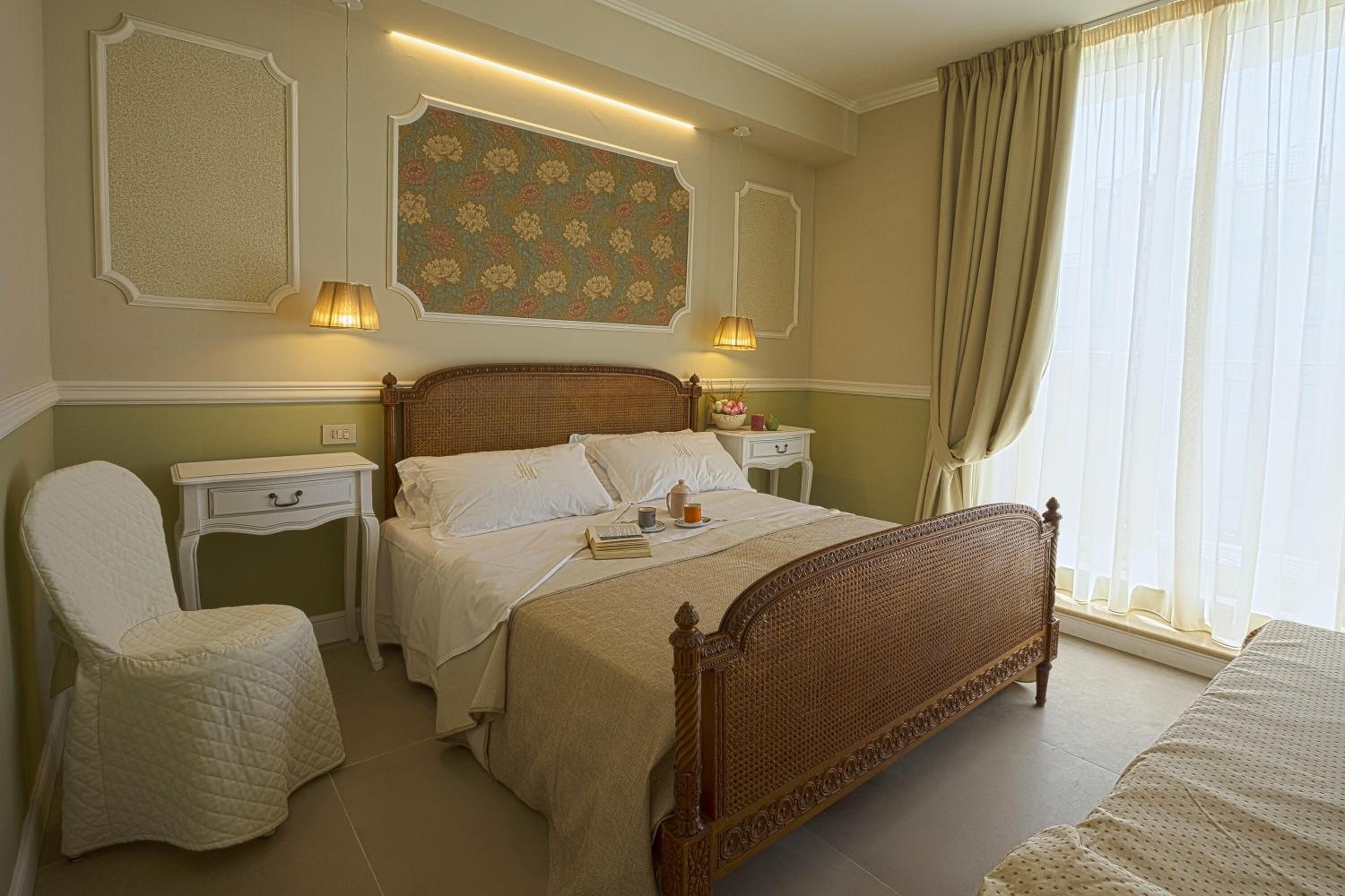 Un dormitorio con una cama grande, mesitas de noche, una silla y un ventanal con cortinas.