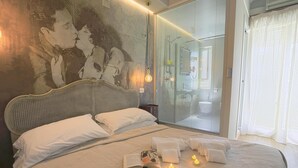 Une chambre avec un grand lit, un miroir fixé au mur et une porte vitrée donnant sur la salle de bain.