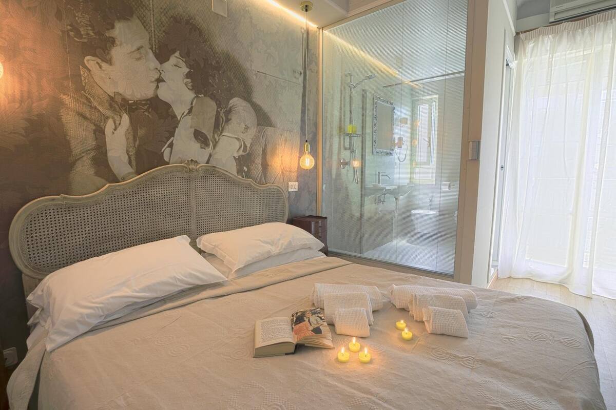 Ein Schlafzimmer mit einem großen Bett, einem Wandspiegel und einer Glastür zum Badezimmer.