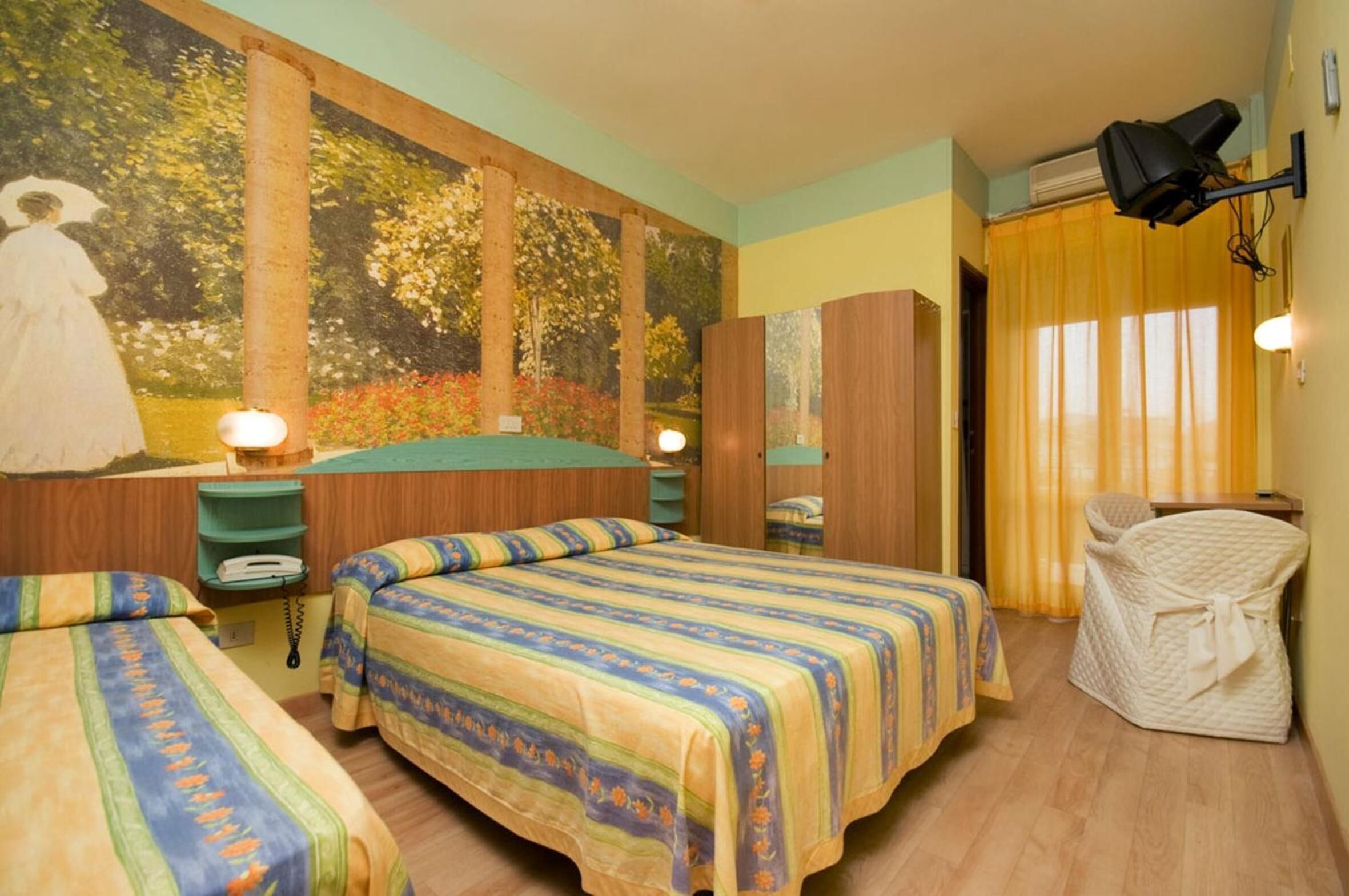 A hotel room with two beds, a large mural, a wardrobe, a chair, and a desk with a lamp.