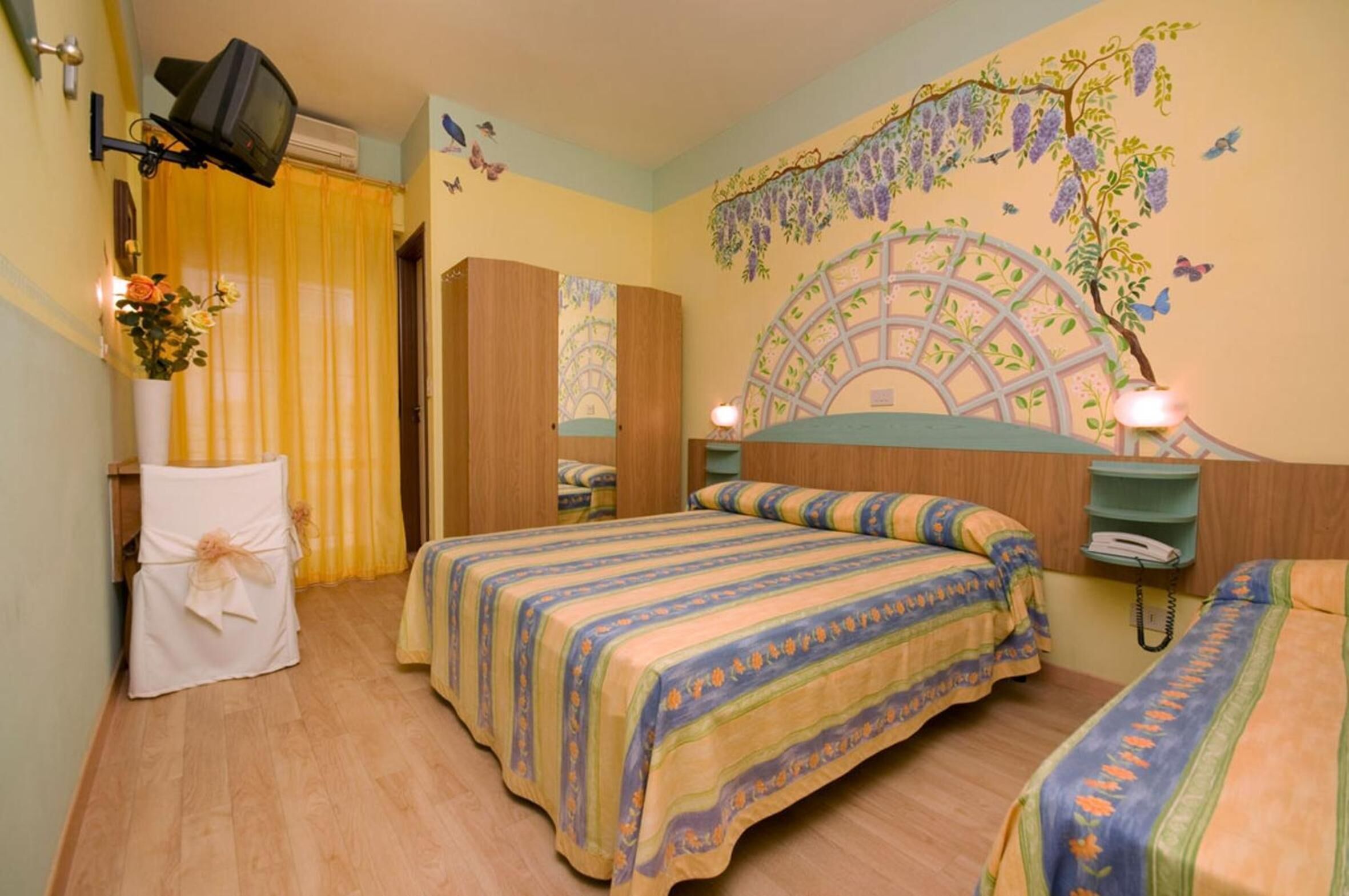 Habitación de hotel con dos camas, televisión, teléfono y un mural decorativo.