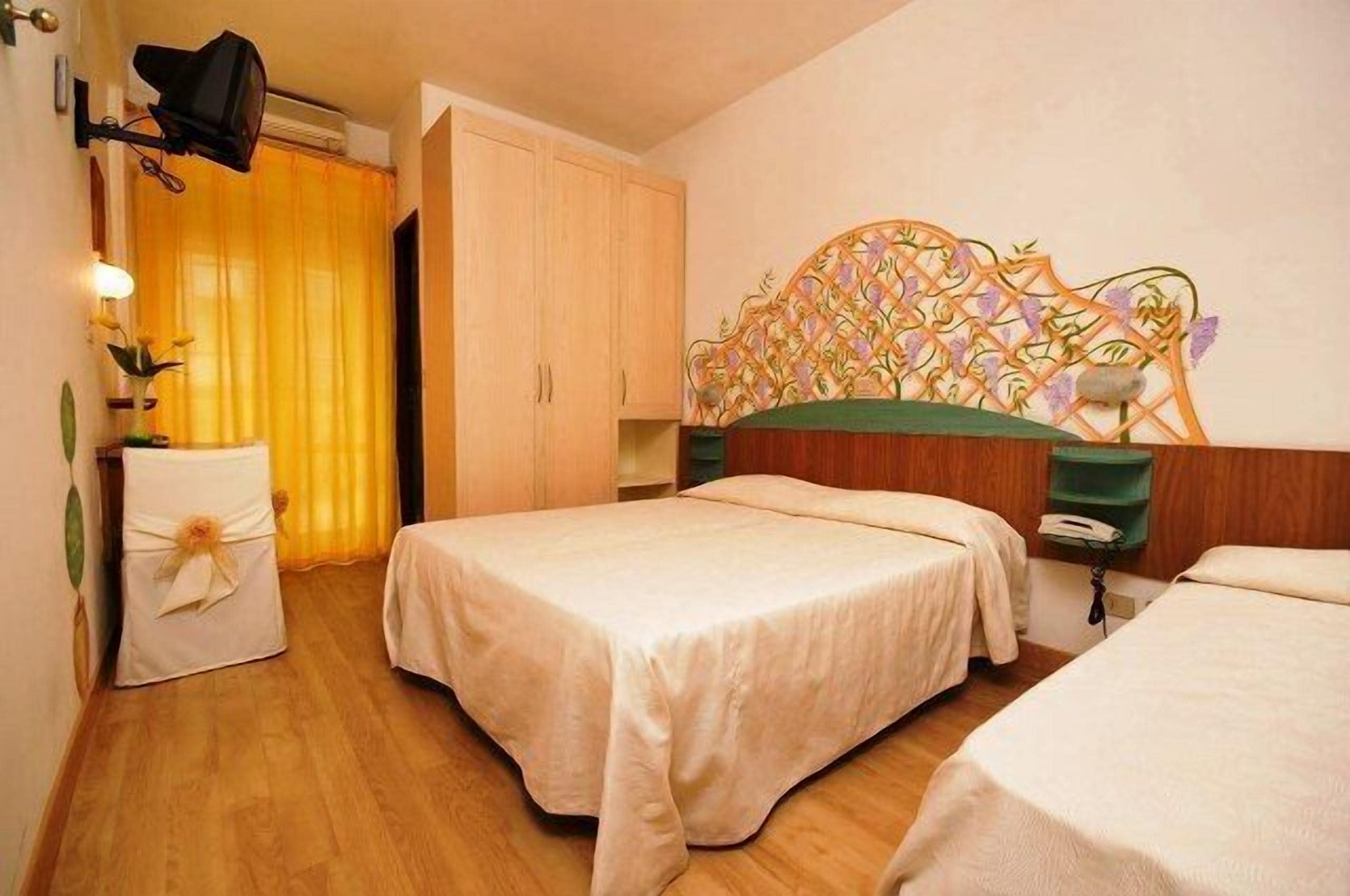 Een hotelkamer met twee bedden, houten vloeren, een decoratief hoofdeinde en een klein nachtkastje met een lamp.