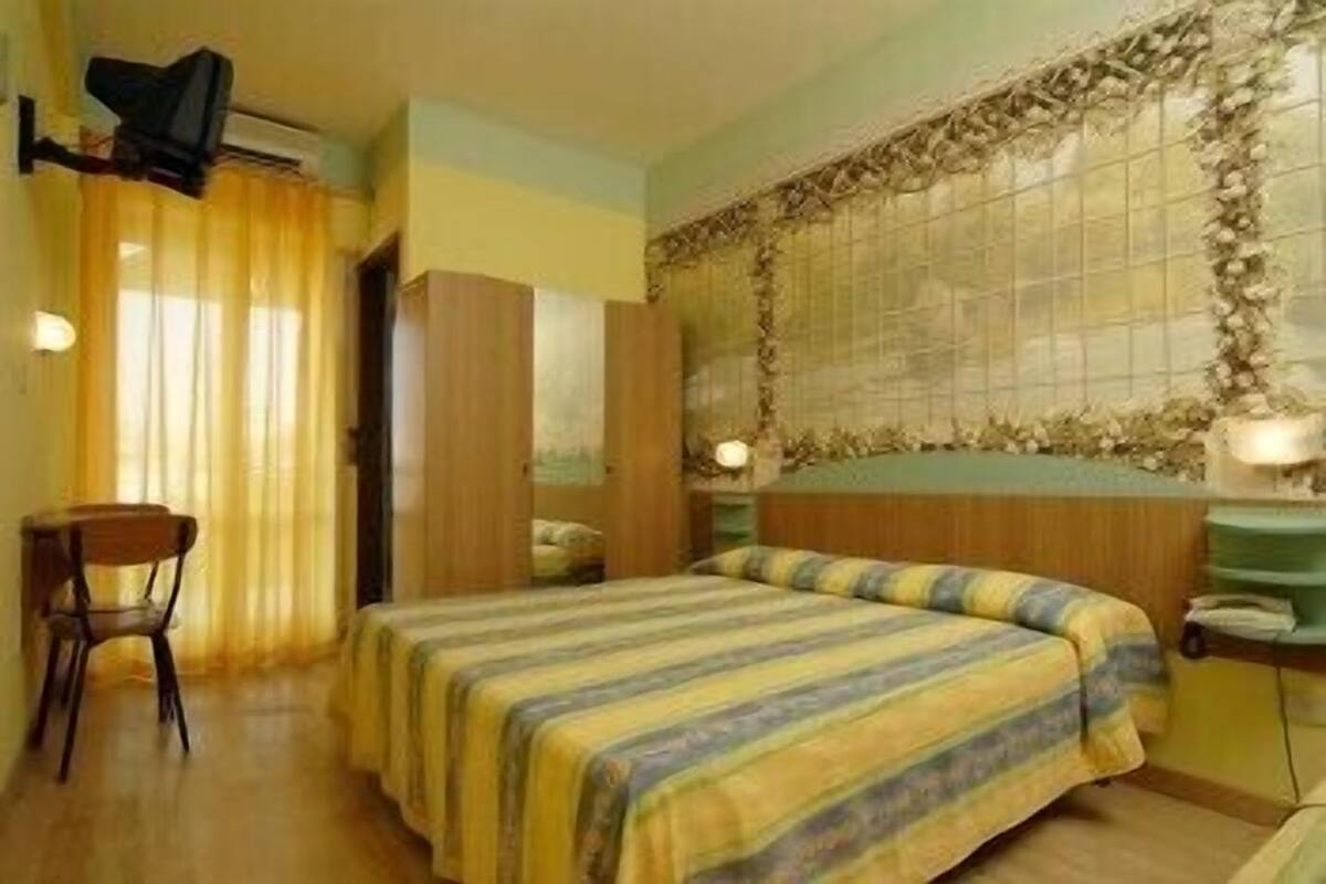 Ein Hotelzimmer mit Bett, Stuhl, Schreibtisch und einem fenster mit Vorhängen.