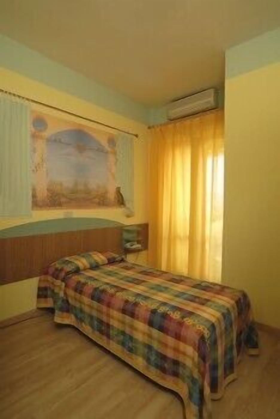 A bedroom with a bed, a nightstand, a painting on the wall, and a window with curtains.