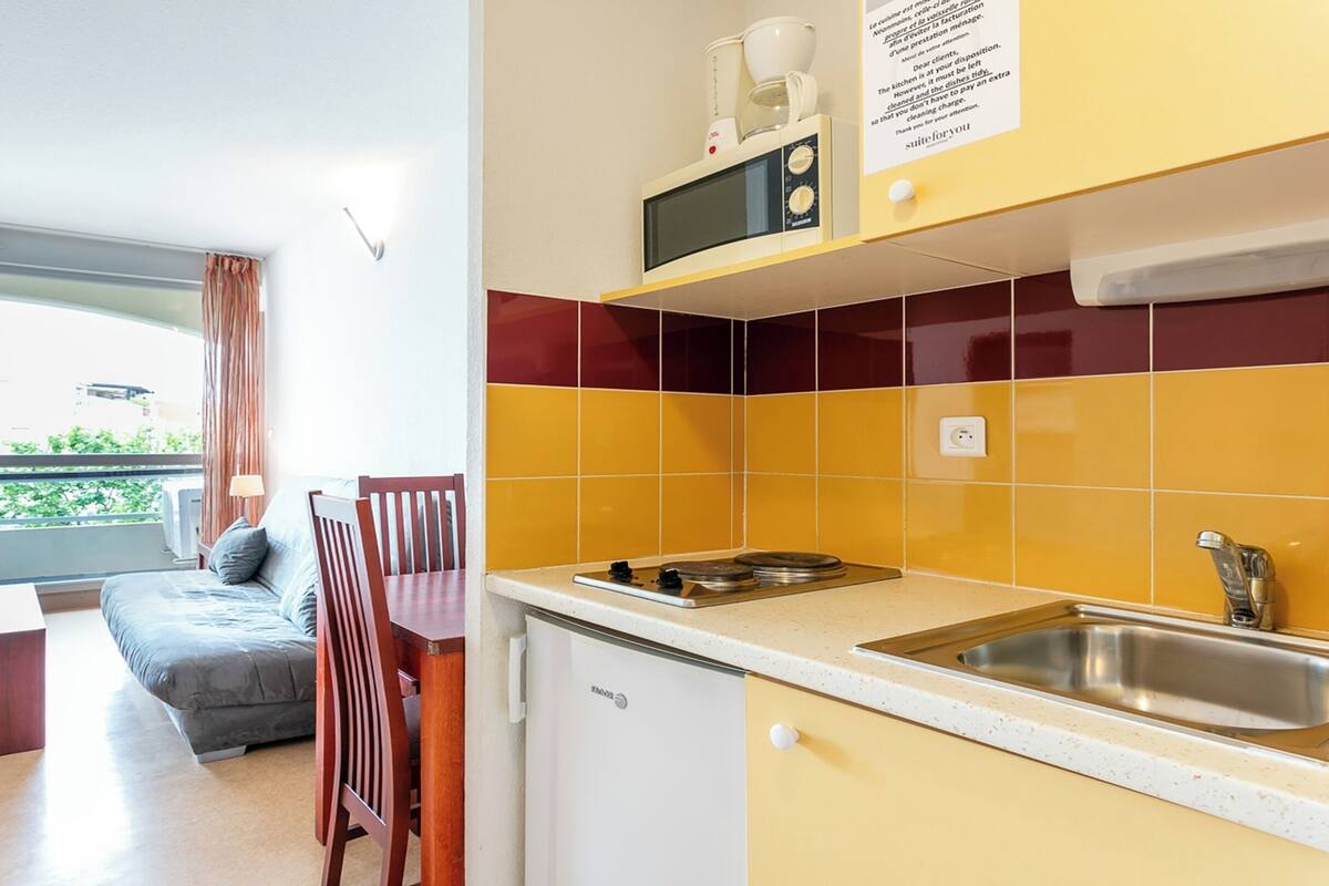 Une cuisine compacte équipée d’un four à micro-ondes, d’un évier et d’un petit réfrigérateur. Un coin repas avec une table et des chaises est également disponible.