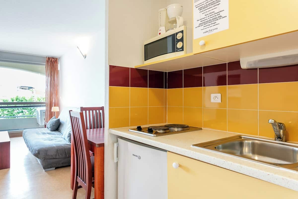 Cocina compacta con microondas, pileta y heladera pequeña. Zona de comedor con mesa y sillas.