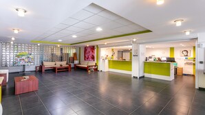 A reception area with a green counter, a waiting area with sofas, and a display wall with magazines.
