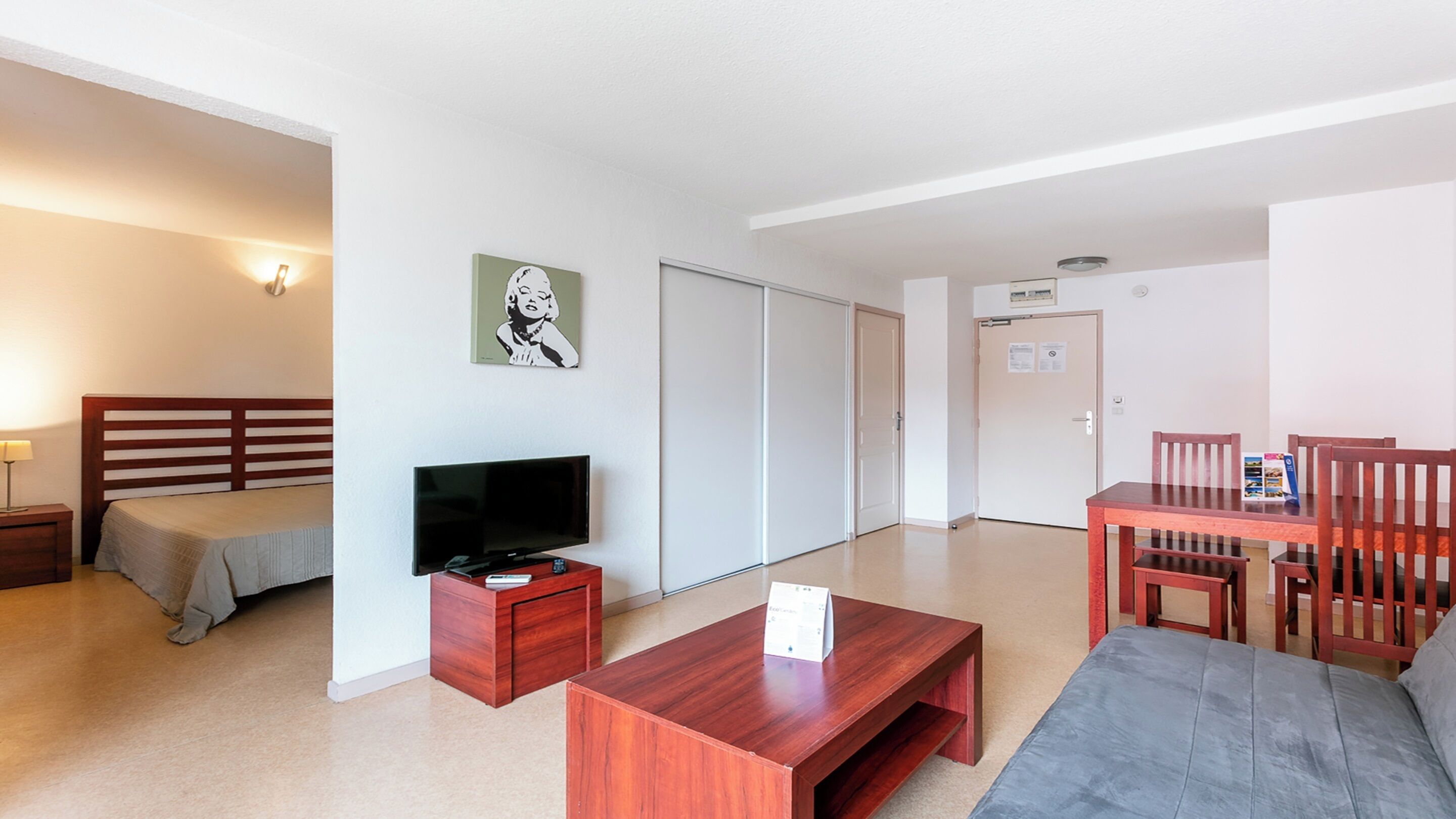 Une chambre d’hôtel comprenant un lit, une télévision, un bureau en bois, un canapé et une table à manger avec des chaises.