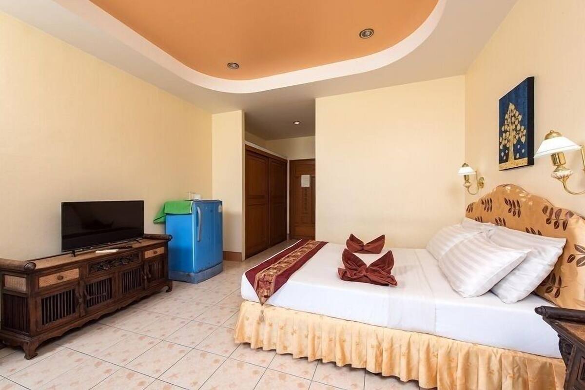 Una habitación de hotel con una cama, televisor, cómoda y un bote de basura azul.