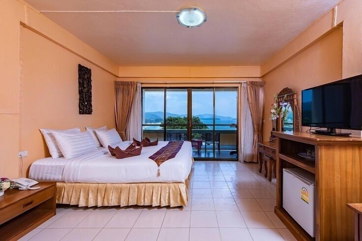 Habitación de hotel con cama, televisor, escritorio y balcón con vistas.