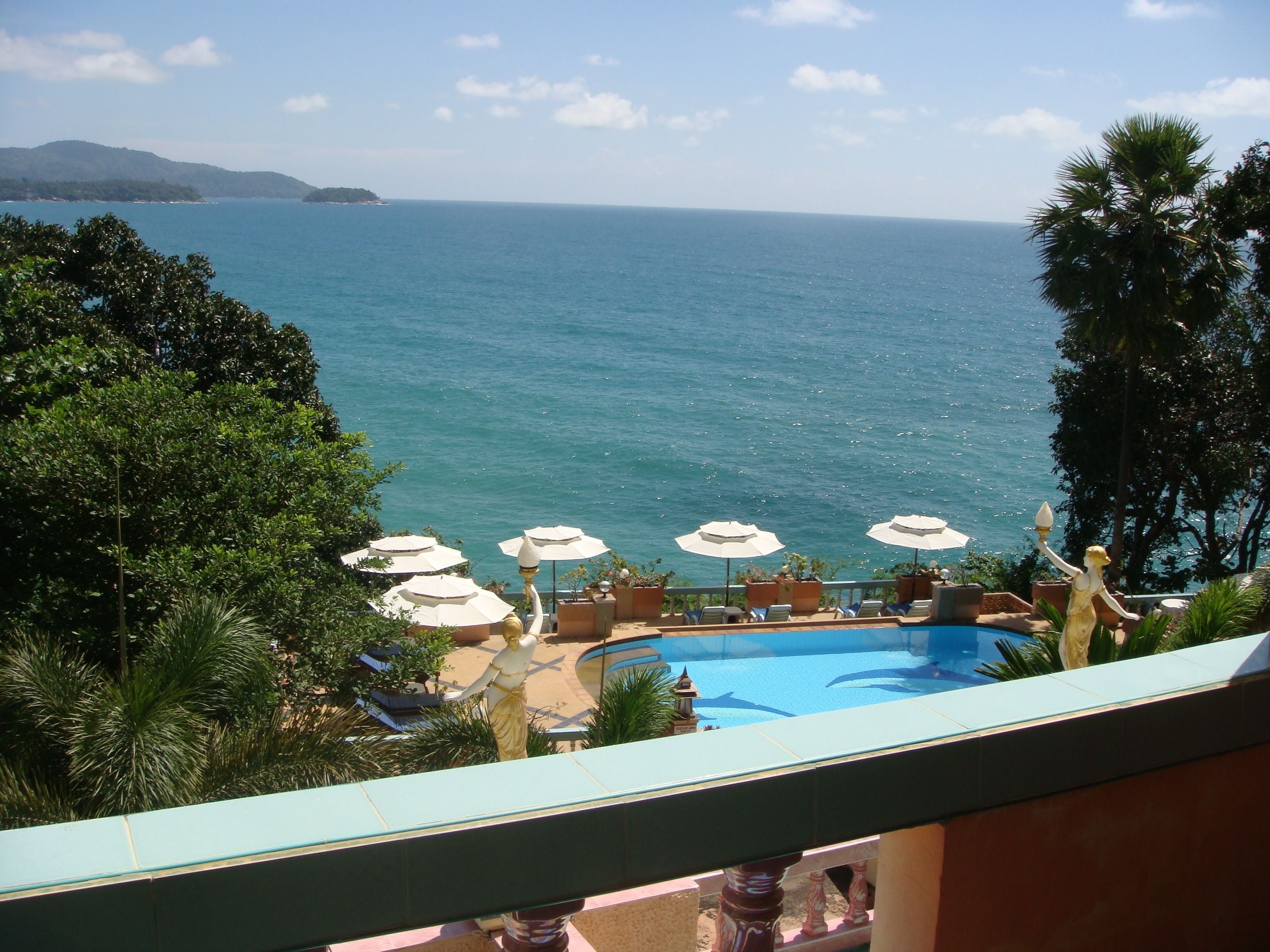 A pool area with umbrellas and lounge chairs, overlooking a body of water and a distant landmass.