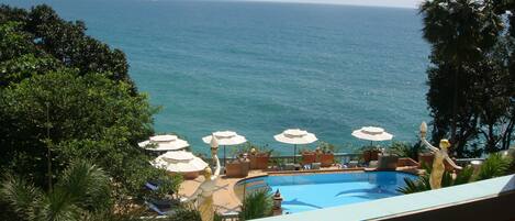 A pool area with umbrellas and lounge chairs, overlooking a body of water and a distant landmass.