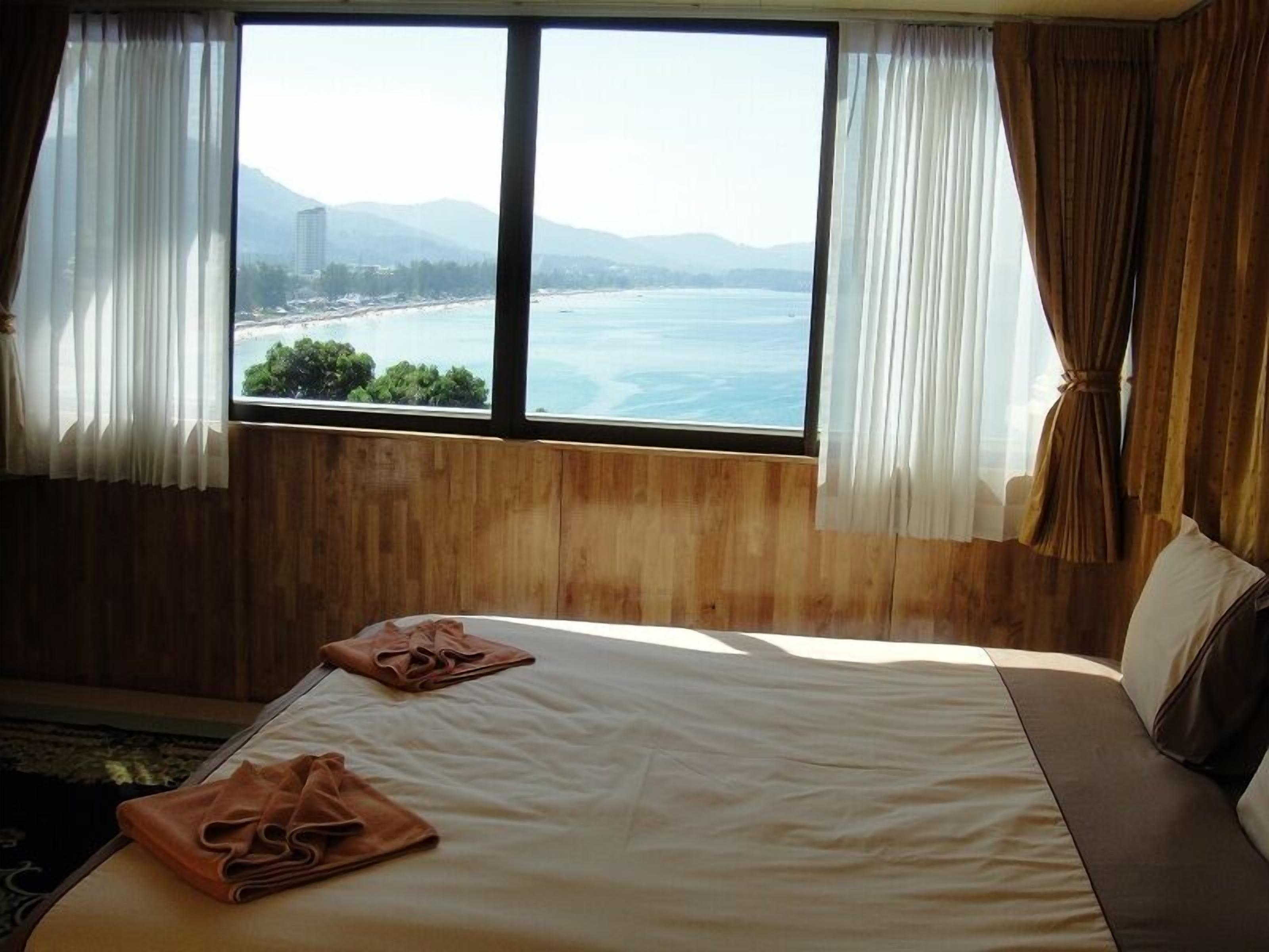 A hotel room with a large bed, two towels, and a view of the sea and mountains.