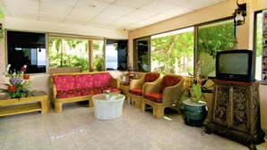 Un salón con sofá, sillas, televisor y ventana con vista a follaje.