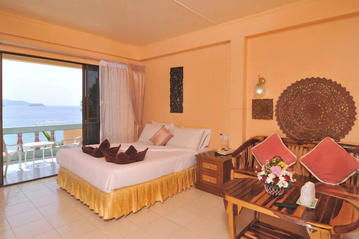 Habitación de hotel con cama, una mesa de comedor de madera con sillas, un balcón y vistas al mar, y decoración en las paredes.