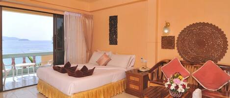 A hotel room with a bed, a wooden dining table with chairs, a balcony with a view of the sea, and decorative wall art.