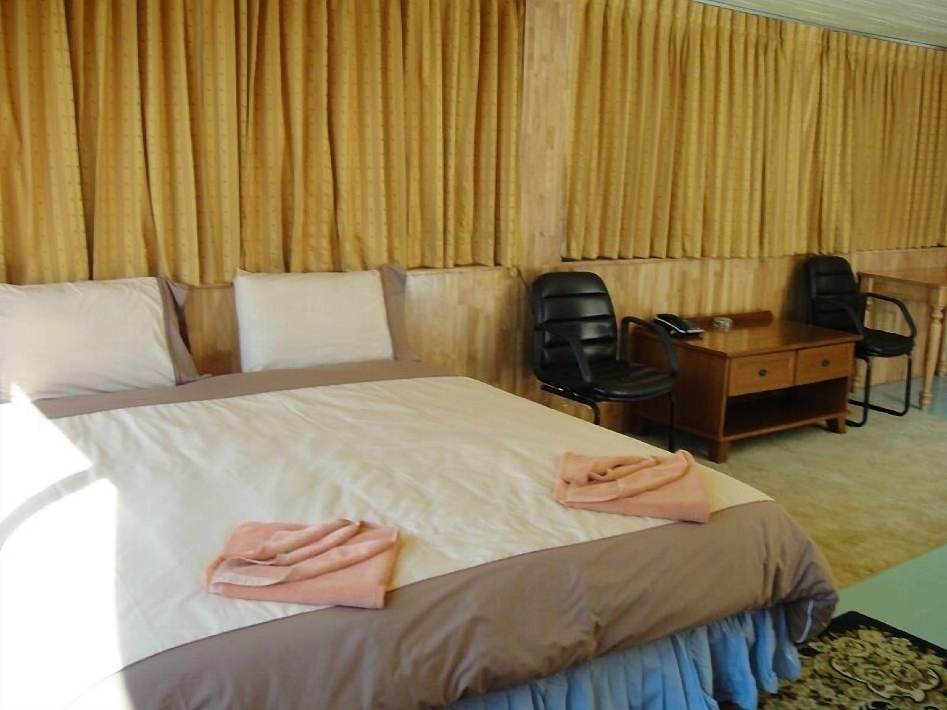 Una habitación de hotel con una cama grande, dos sillas negras, un escritorio de madera y una lámpara.