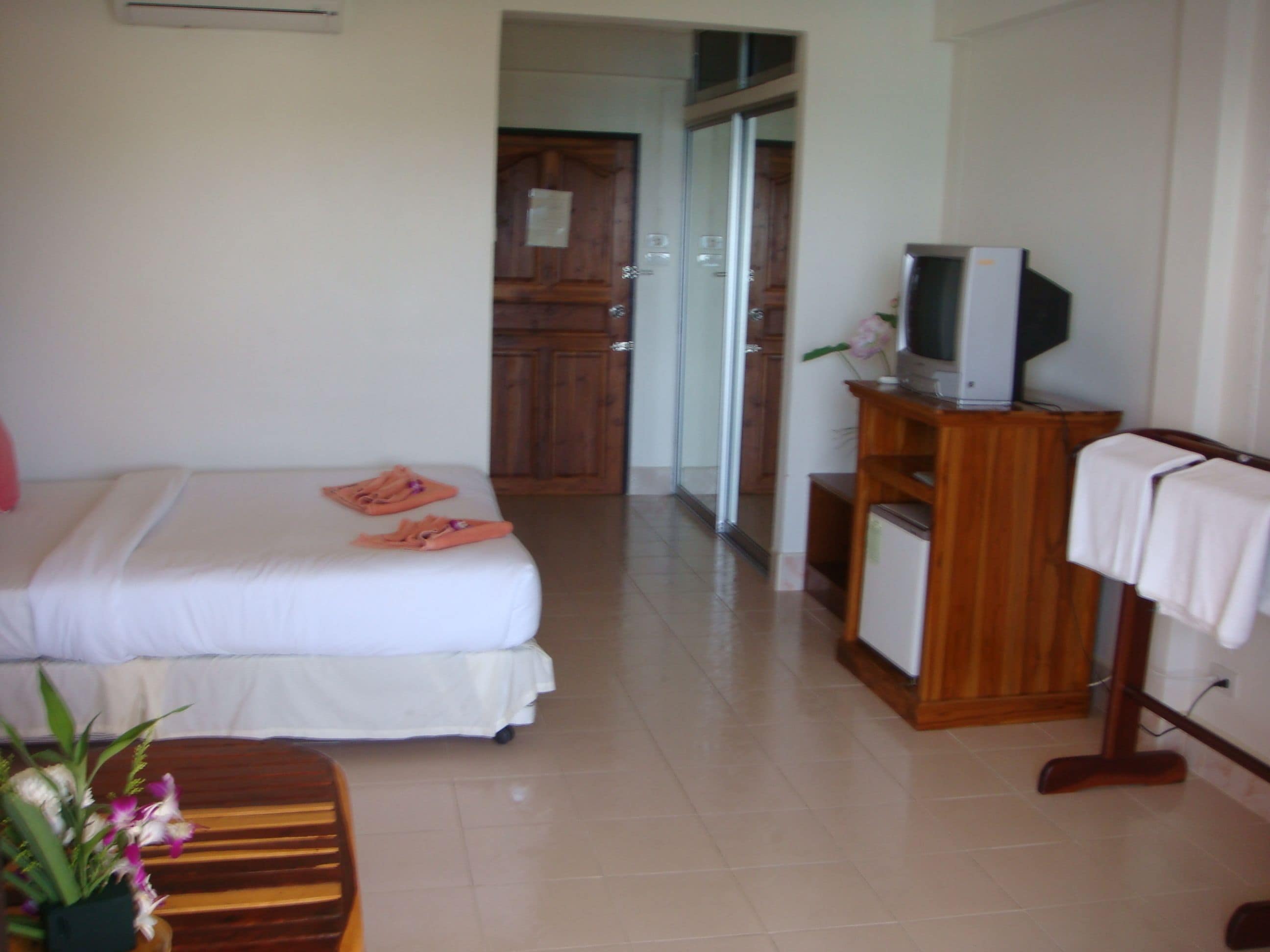 A hotel room with a bed, a television on a wooden stand, and a bathroom visible through a glass door.
