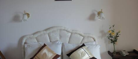 Un lit bien fait, doté d’une tête de lit capitonnée, de deux coussins décoratifs, d’une œuvre d’art encadrée accrochée au mur et d’une petite table sur laquelle est posé un vase de fleurs.