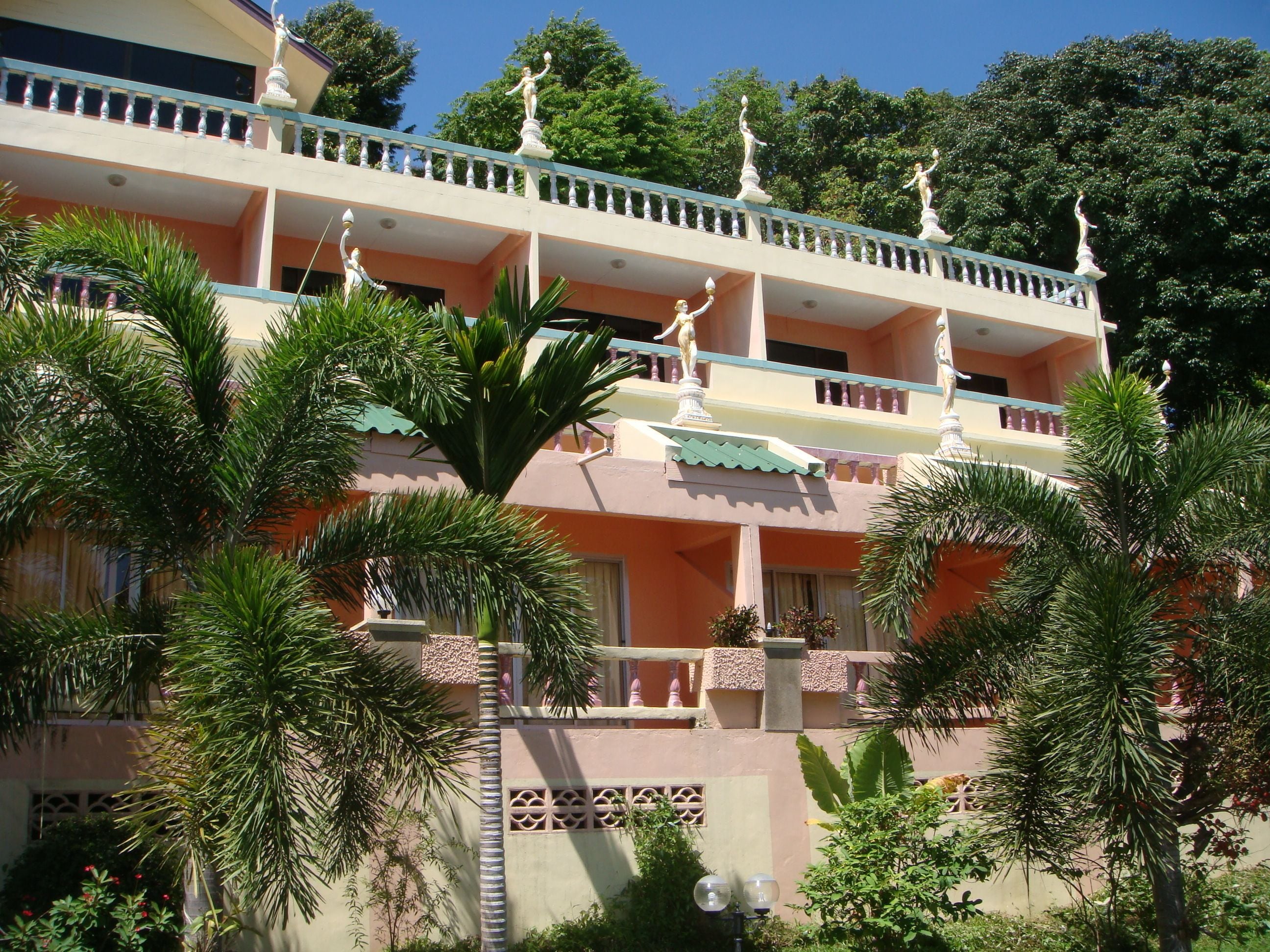 A multi-story building with balconies, palm trees, and statues.