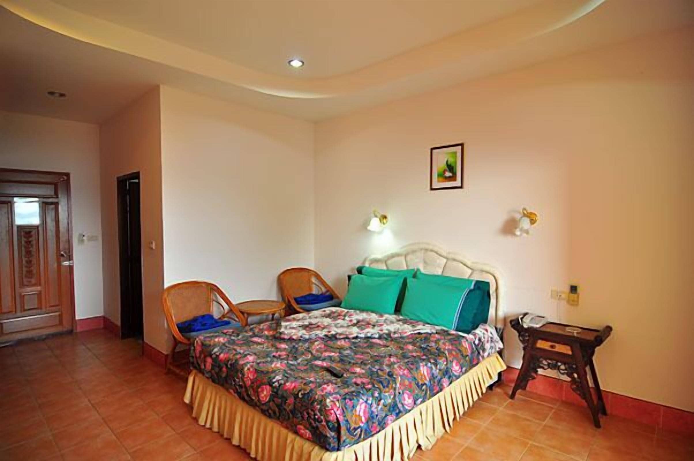 A bedroom with a bed, two chairs, a small table, a nightstand, and a door.