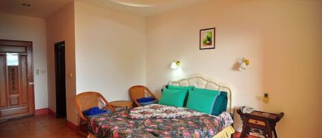 A bedroom with a bed, two chairs, a small table, a nightstand, and a door.