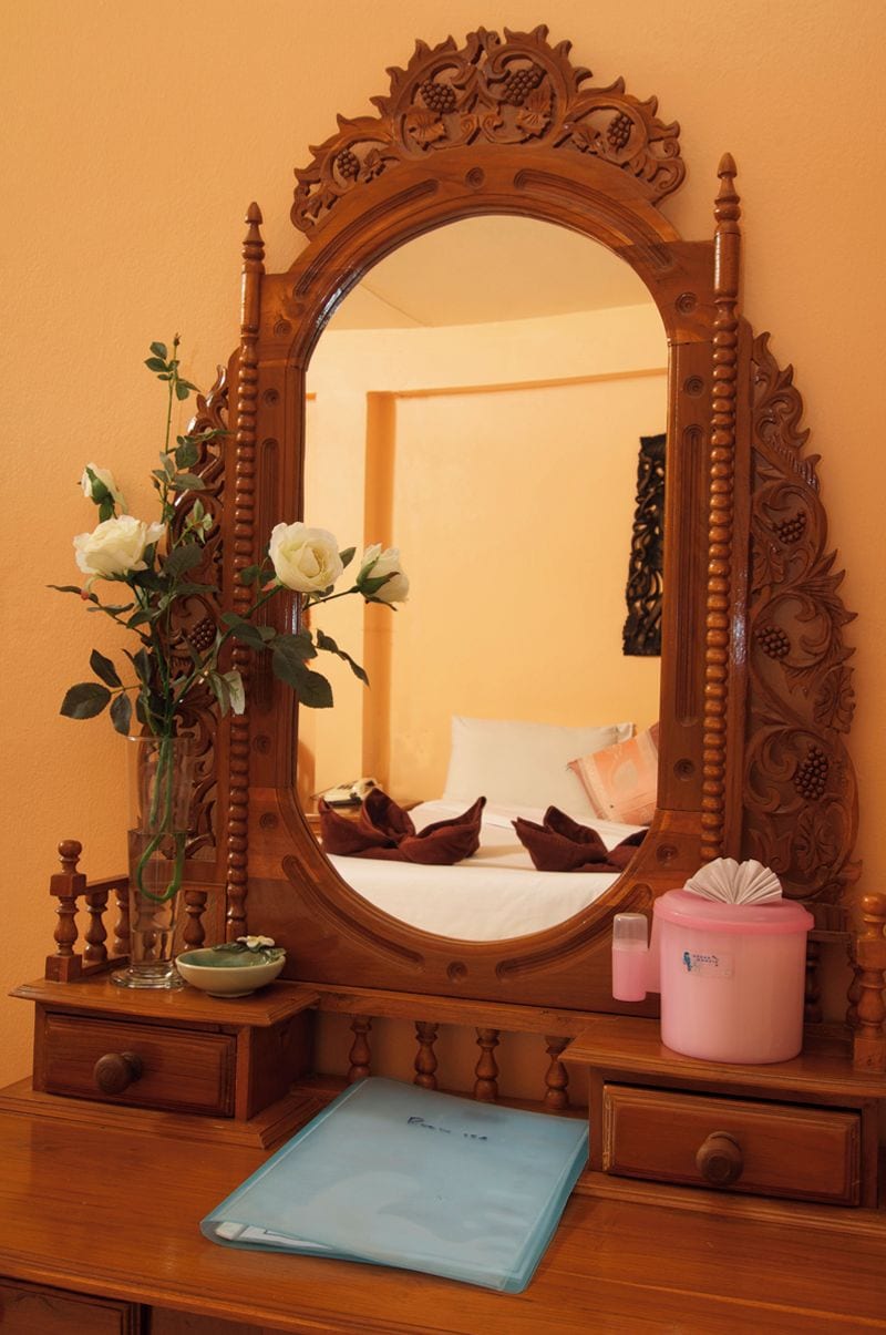 Une commode en bois avec un miroir, un vase avec des fleurs blanches, une boîte de mouchoirs et un dossier bleu.