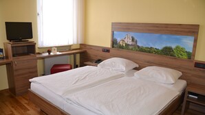 Habitación de hotel con una cama de madera, un escritorio con una computadora, un televisor y un cuadro en la pared.