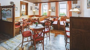 Un restaurant doté de meubles en bois, de nombreuses tables et chaises, et de grandes fenêtres avec des rideaux.