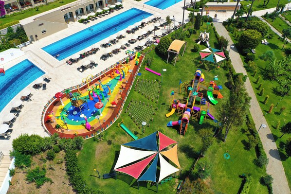 Ein Luftbild eines Resorts mit mehreren Schwimmbecken, einem Spielbereich für Kinder und einem gepflegten Garten.