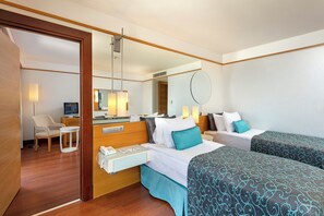 Habitación de hotel con piso de madera, un escritorio con lámpara, una silla, cama con ropa de cama estampada, una mesita de noche con teléfono y un espejo en la pared.