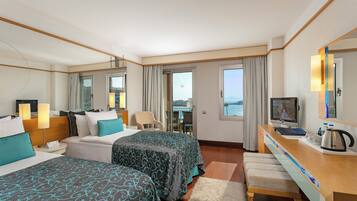 Quarto de hotel com duas camas, uma mesa de trabalho com televisão, uma cadeira e vista para o mar.