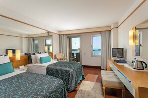 Ein Hotelzimmer mit zwei Betten, einem Schreibtisch mit Fernseher, einem Sessel und Meerblick.
