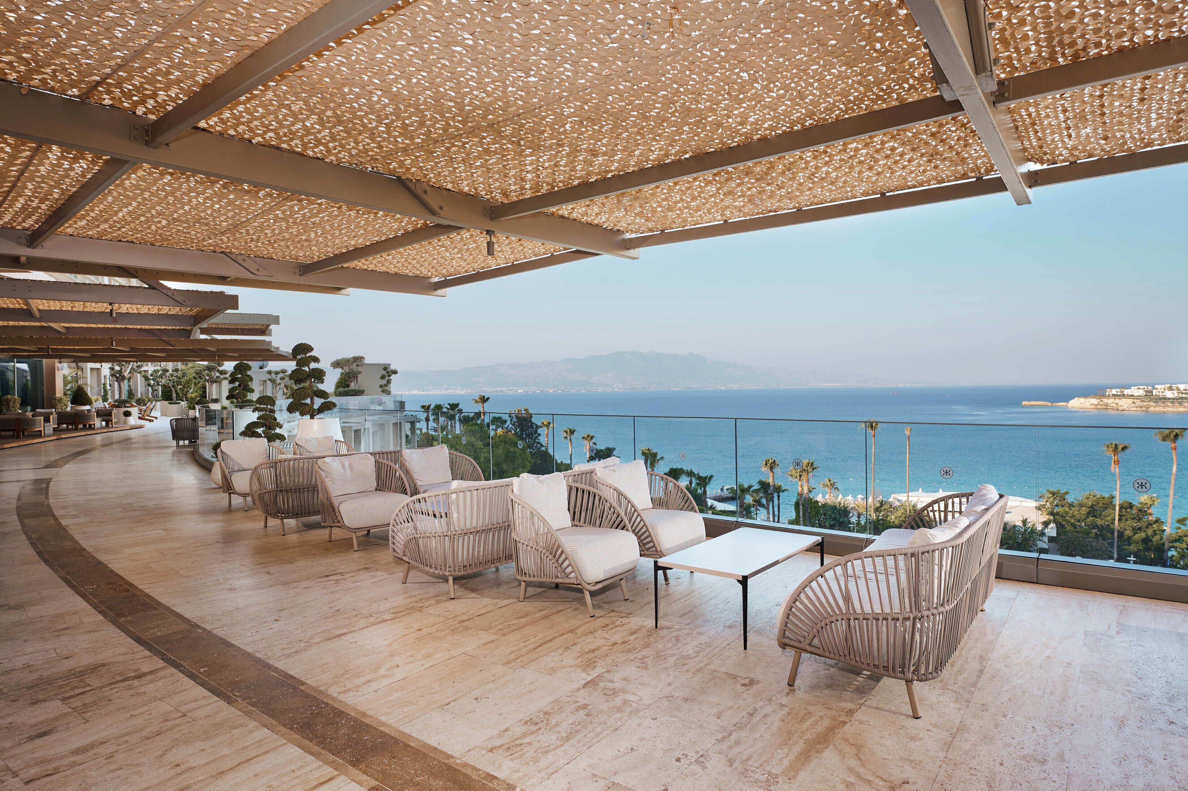 A terrace with wicker furniture, a glass balustrade, and a view of the sea.