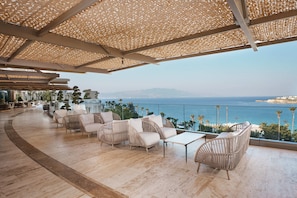 Una terraza con mobiliario de mimbre, barandilla de vidrio y vista al mar.