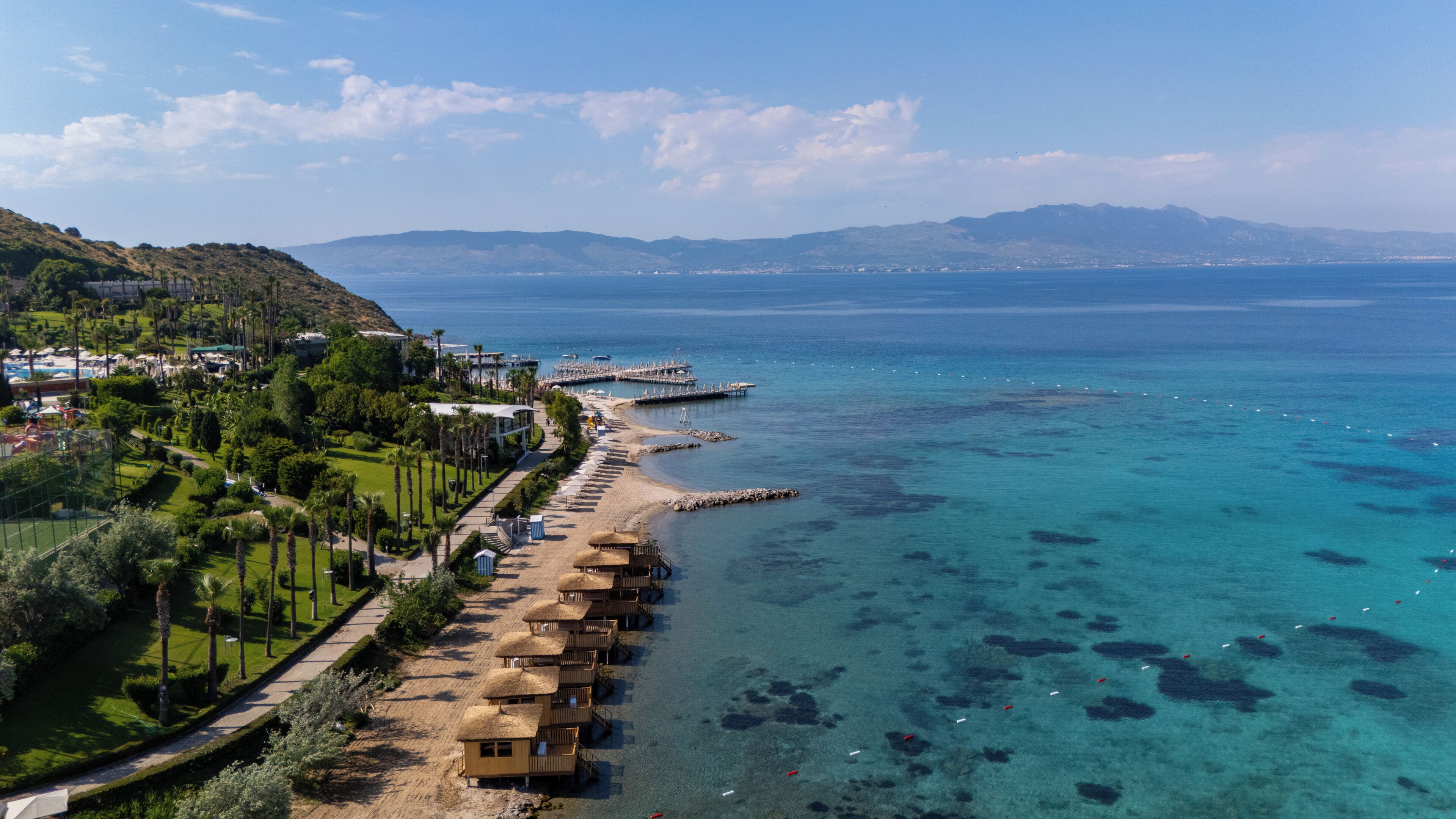 Un resort costero con bungalows sobre el agua, un puerto deportivo y una vista despejada del mar.