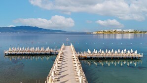 A pier extending into calm waters with rows of sun loungers and umbrellas, a distant shoreline, and a clear sky. - Kefaluka Resort - All Inclusive (Bodrum)