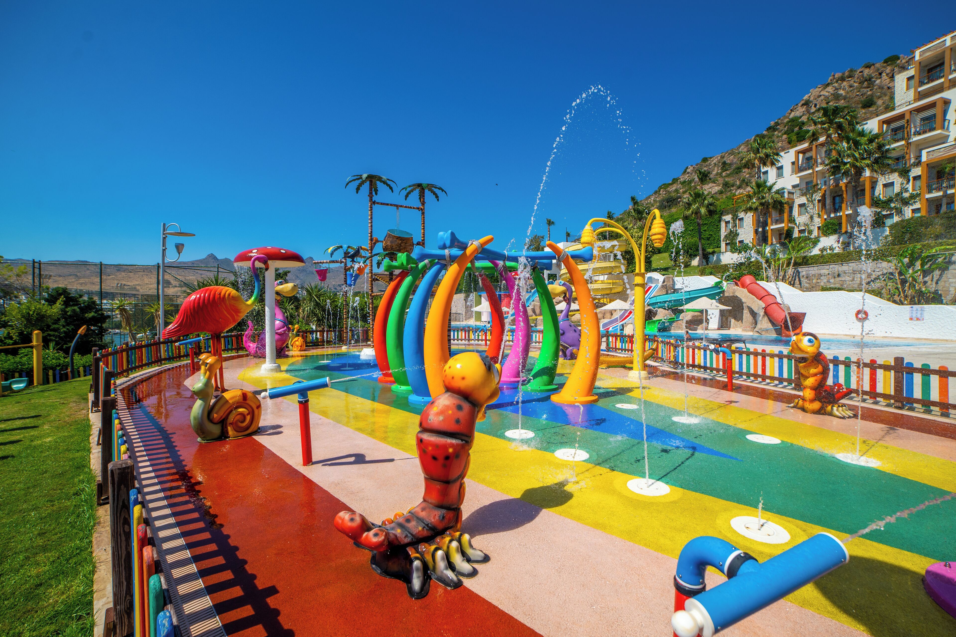Ein farbenfroher Wasserpark mit Rutsche, Raupe-Spielgerät und Schwimmbecken.