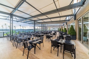 An outdoor dining area with tables and chairs, large windows, and a view of the water. - Kefaluka Resort - All Inclusive (Bodrum)