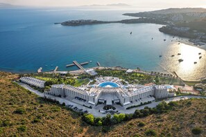 Ein großes Hotel mit einem zentral gelegenen Schwimmbad, mehreren Parkplätzen und Blick auf das Meer.