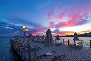 A wooden pier with lounge chairs and umbrellas, a sign reading 'KEFALUKA At the Edge of Calm,' and a sunset over the water. - Kefaluka Resort - All Inclusive (Bodrum)